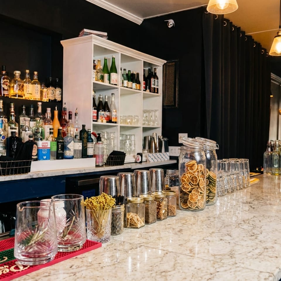 Well-stocked restaurant bar with liquor bottles, citrus fruit, glassware, cocktail ingredients, and warm pendant lighting.